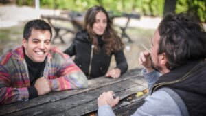Group of relaxed and smiling happy young friends, female and male, smoking cannabis marijuana ganja or hashish joint in public park outdoor. Young people smoke thc grass. Real life scene concept