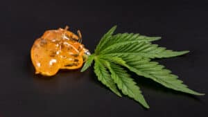 high thc, pieces of golden yellow cannabis wax and green leaf, marijuana concentrate on dark backround