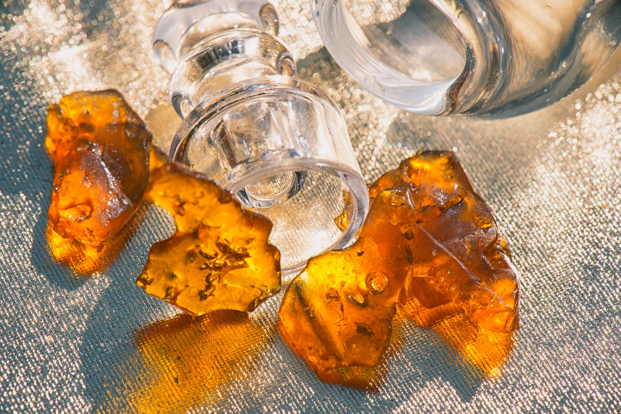 Pieces of cannabis oil concentrate aka shatter with glass rig over sparkling background